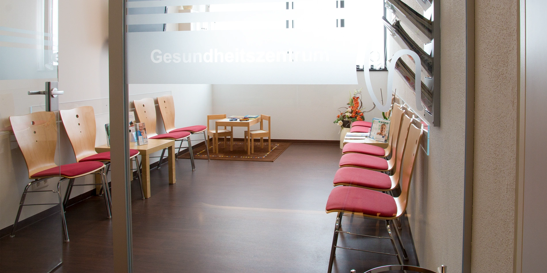 Wartebereich des Gesundheitszentrums mit roten Stühlen und Spieltisch für Kinder
