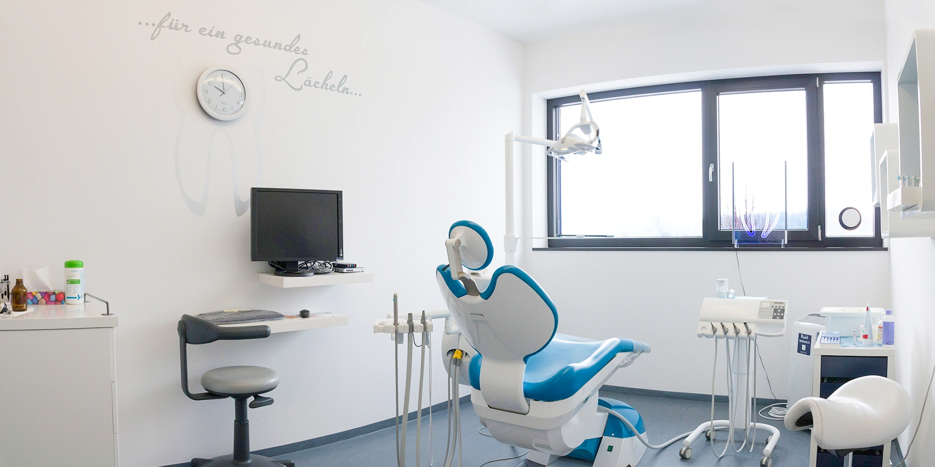 Behandlungszimmer mit blauem Zahnarztstuhl und Wandtattoo "für ein gesundes Lächeln" in der Praxis Dr. Raicov
