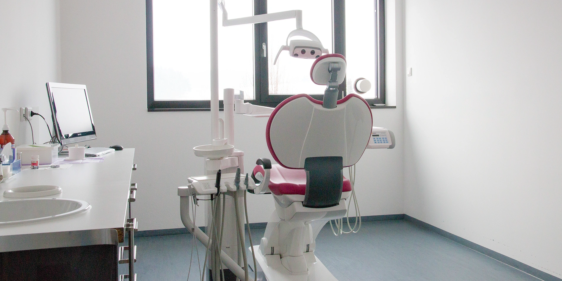Modern eingerichtetes Behandlungszimmer der Zahnarztpraxis Dr. Raicov mit Untersuchungsstuhl am Fenster mit Blick ins Grüne